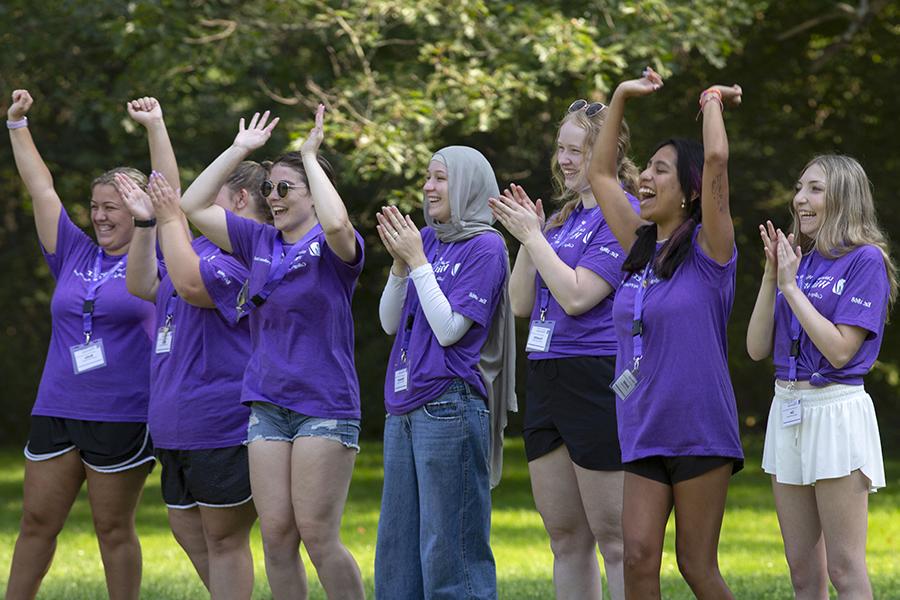 A group of students wear purple shirts and raise their arms as they cheer each other on during a leadership exercise.