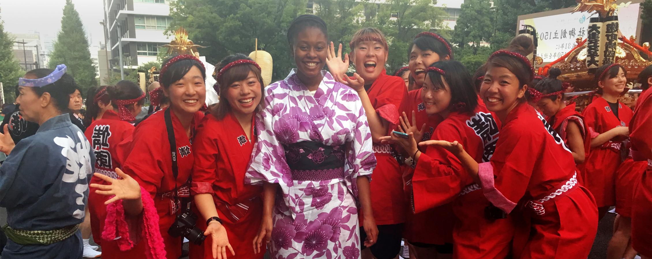 An African American female stands in a crowd of smiling people in Japan.